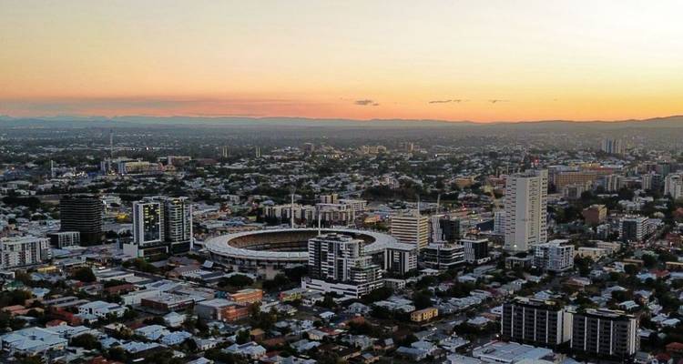 Citywide sunset view featuring a circular stadium surrounded by mid-rise buildings and mountains in distance.
