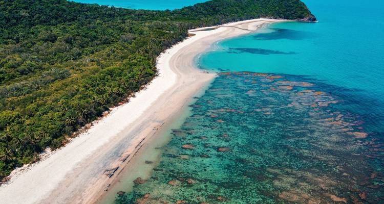 Aerial of a pristine tropical beach bordering turquoise reef waters and dense coastal forest.