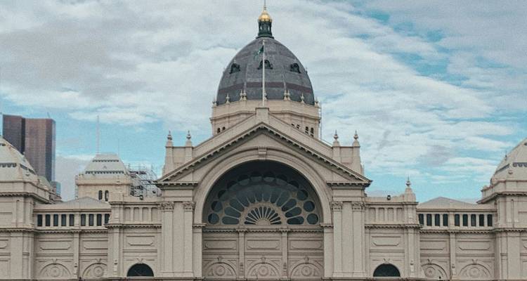 Front façade of Melbourne’s Royal Exhibition Building with ornate dome under partly cloudy sky.