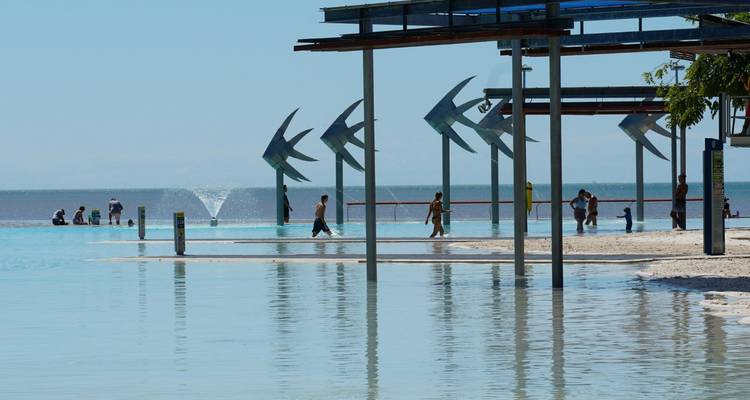 Public lagoon in Cairns with metal fish sculptures and people swimming and relaxing