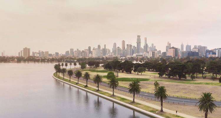 Zacht verlichte panorama van de skyline van Melbourne voorbij het Albert Park Lake omzoomd met palmbomen.