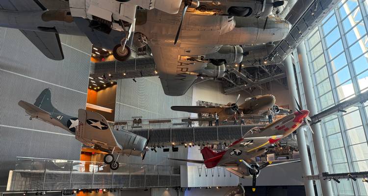 Intérieur d'une galerie aéronautique avec plusieurs aéronefs de l'époque de la Seconde Guerre mondiale suspendus au plafond.