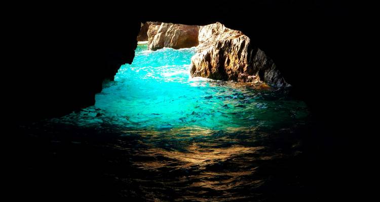 Sunlit turquoise water glows at the entrance of a dark sea cave.