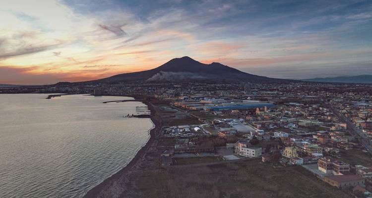 Aerial sunset view of Mount Vesuvius looming over coastal suburbs and the bay.