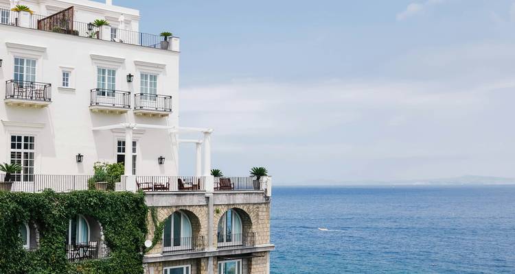 Elegant white seaside villa draped in ivy overlooks the calm blue Mediterranean.