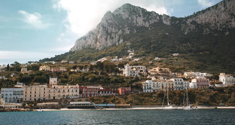 Coastal town of Capri with colorful buildings nestled below a steep green mountain.