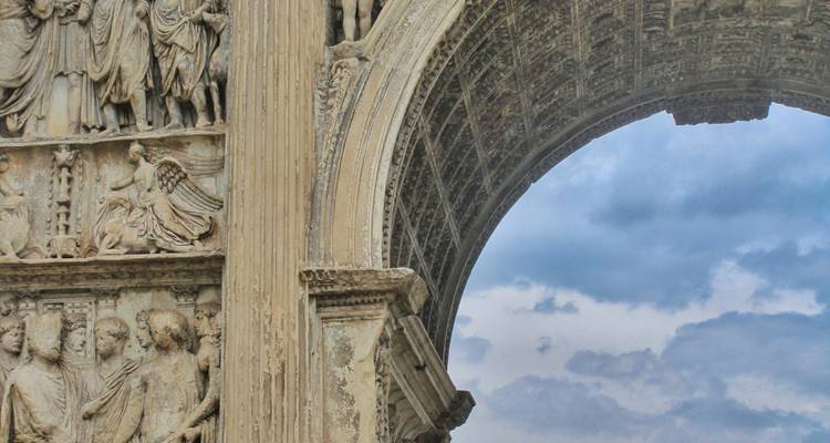 Gedetailleerde gesneden reliëfs en een gewelfde doorgang van de oude Boog van Trajanus tegen een bewolkte lucht.