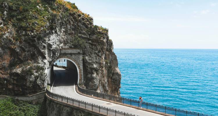 Kustweg tunnel uitgehouwen in de rots naast de felblauwe Middellandse Zee met een eenzame fietser.