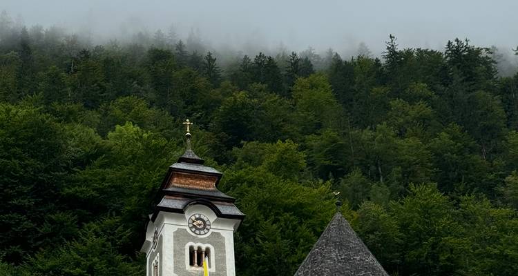 Une petite tour d'église alpine et un toit en ardoise abrupt se dressant contre un versant boisé luxuriant avec du brouillard bas.