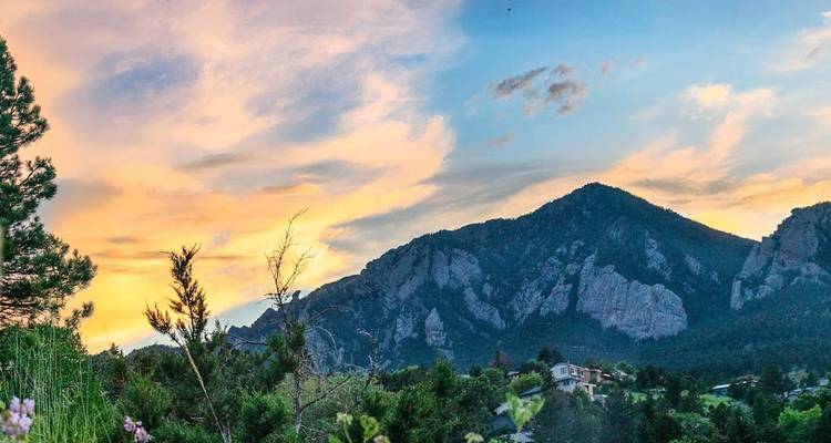 Colorful sunset sky illuminating forested hills and rocky ridges above a small valley community.
