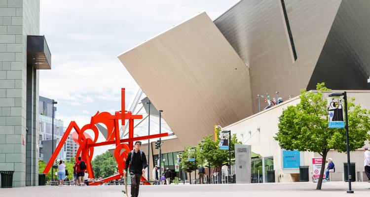 View of the Denver Art Museum's angular architecture with red sculpture in foreground and visitors nearby.