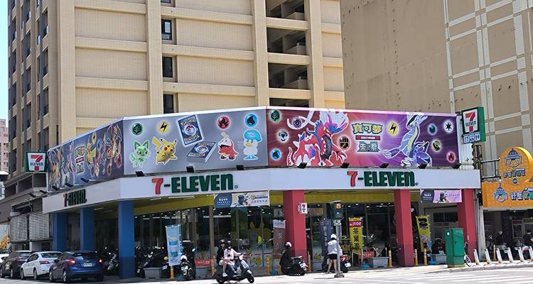 Frente de tienda 7-ELEVEN con temática de Pokémon en una esquina concurrida de la ciudad con conductores de scooters pasando