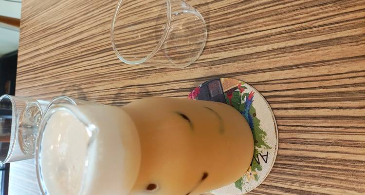 Café helado con leche y espuma en la parte superior servido en una mesa de madera junto a vasos vacíos.