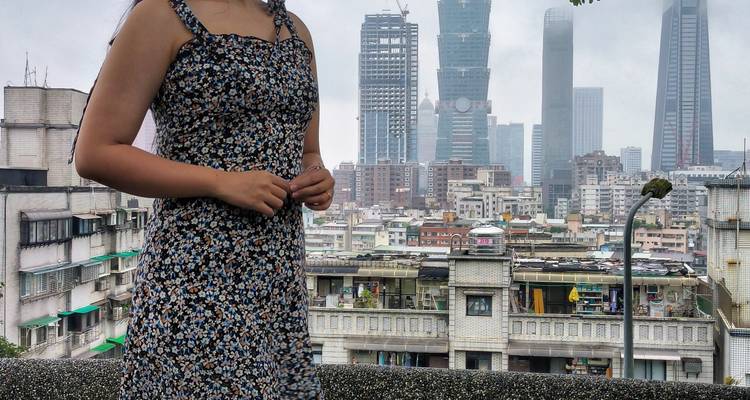 Mujer con vestido floral con el skyline de Taipei y el Taipei 101 elevándose en el fondo nebuloso.
