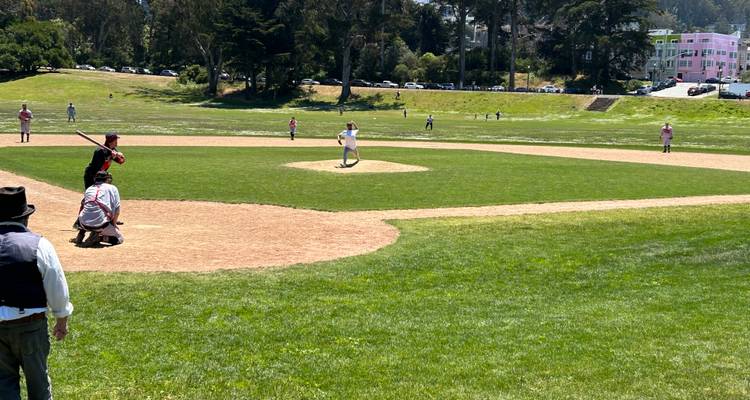 Vintage-style baseball game on grassy field with players in period uniforms