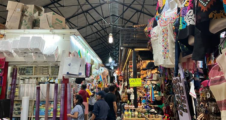 Bustling indoor market aisle filled with colorful textiles, souvenirs and shoppers beneath a high metal roof