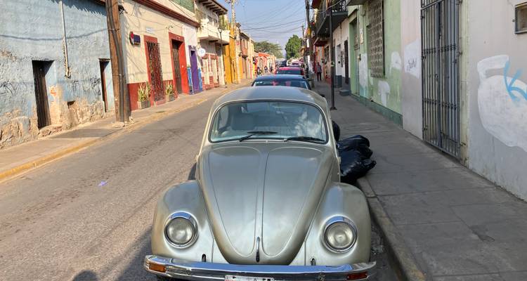Vintage silver Volkswagen Beetle parked on a narrow colonial street lined with colorful buildings