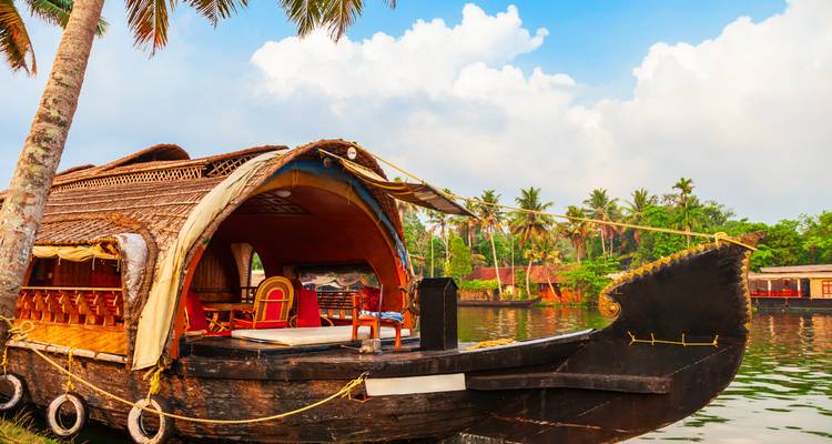 Bote tradicional de Kerala con frente abierto y techo de paja amarrado a lo largo de un canal verde y exuberante.