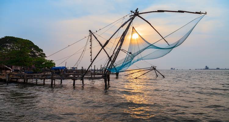 Redes de pesca chinas recortadas contra el Mar Arábigo al atardecer con un cielo dorado.