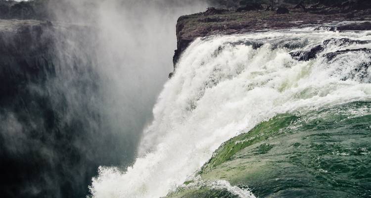 Massive curtain of water plunging over edge of Victoria Falls into misty gorge.