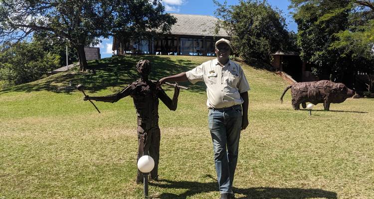 Guide de lodge de safari posant de manière ludique avec une sculpture métallique sur une pelouse herbacée.