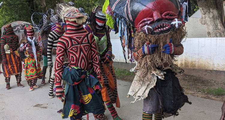 Des danseurs portant des masques, vêtus de costumes en tricot aux couleurs vives, défilent dans une rue en portant de hauts couvre-chefs.