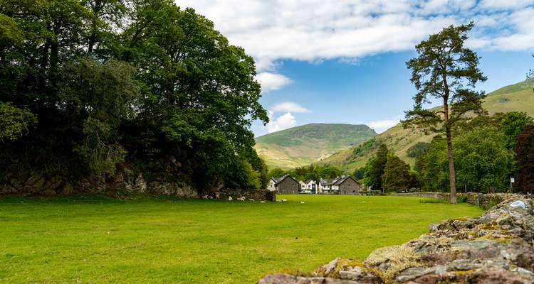 Green pasture with stone wall and distant cottages beneath rolling hills.