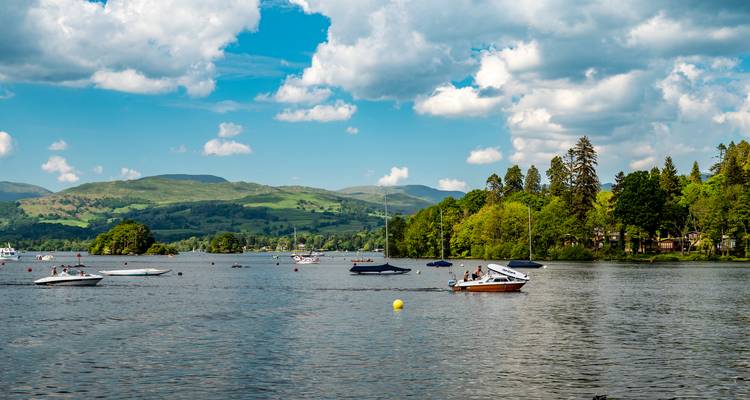 Busy lake with small motorboats under bright blue sky and green hills beyond.