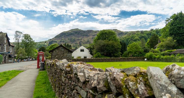 Stone wall and red phone box lead into village street with mountain backdrop.