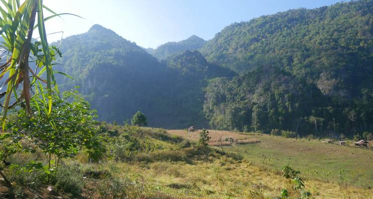 Open grassy valley backed by steep forested cliffs and hazy mountain peaks.