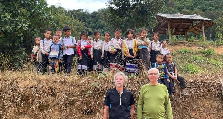 Line of local schoolchildren pose on a berm behind two adult travellers in a rural setting.