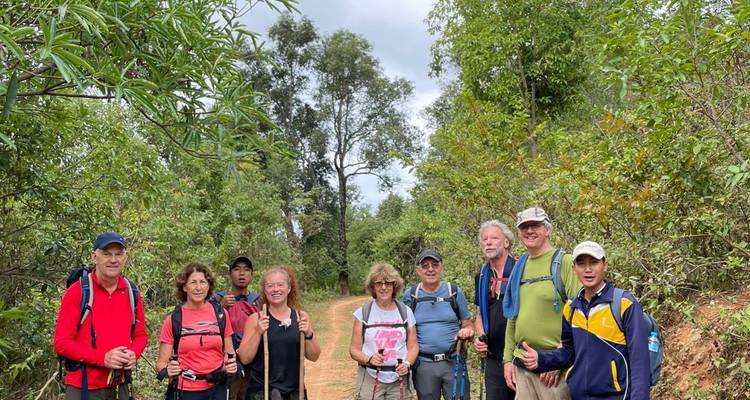 Group of hikers smile for a photo on a dirt trail flanked by dense green shrubs.