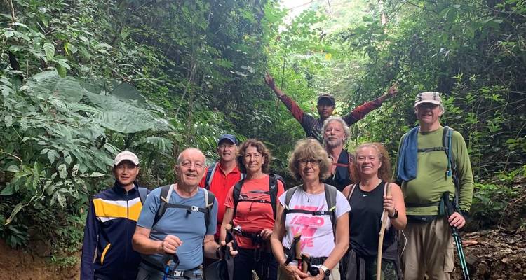Group of trekkers pose under shaded forest canopy, one member raising arms in celebration.