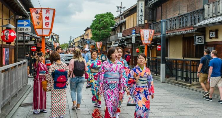 Eine Menschenmenge von Besuchern in farbenfrohen Yukatas schlendert durch Kyotos traditionelle Holzstraße, die mit Laternen gesäumt ist.
