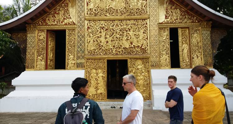 Visitors converse outside an ornate gold-decorated temple facade in Luang Prabang.