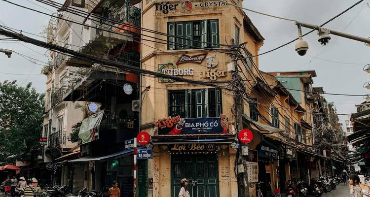Weathered colonial-era corner building covered in bar signs and tangled electric cables in Hanoi’s Old Quarter.