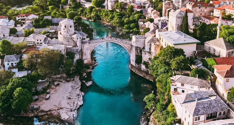Vue aérienne du pont de pierre emblématique de Mostar s'arquant au-dessus des eaux turquoise du fleuve et de la vieille ville.