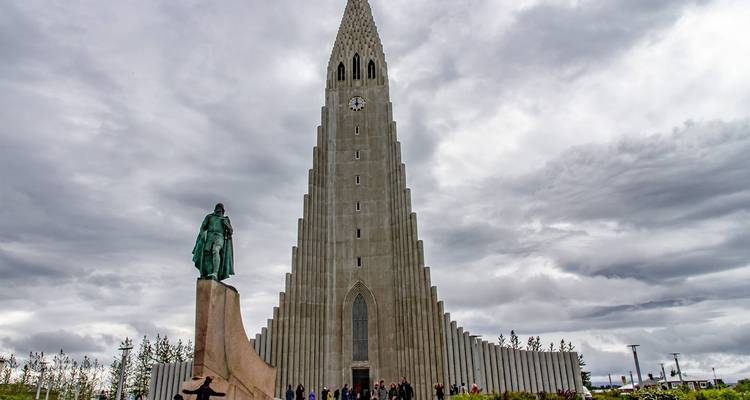 Hallgrimskirkja und Leif-Erikson-Statue unter dramatischen grauen Wolken mit Touristen, die am Eingang versammelt sind