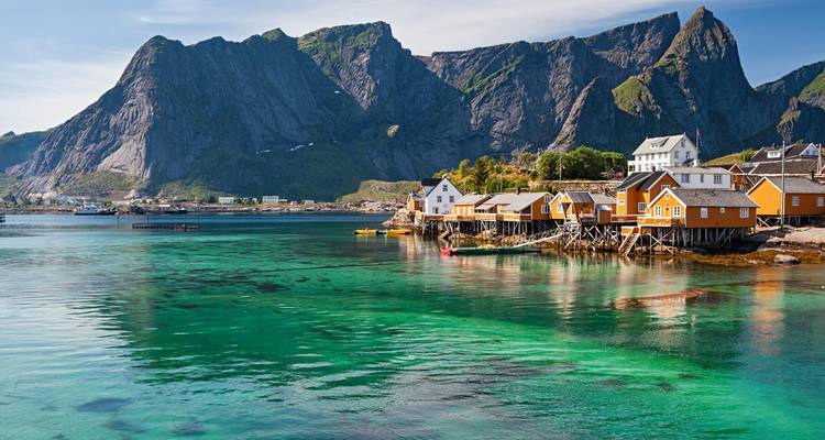 Bahía de un turquesa cristalino con cabañas rorbuer amarillas y picos dentados y majestuosos en Lofoten