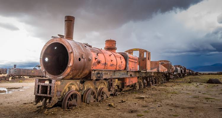 Rusting locomotives lined up in the Train Cemetery under dramatic storm clouds near Uyuni