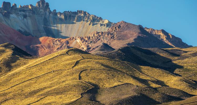Sun-lit ridges of multicolored Andean mountain with sharp rock crest against clear blue sky