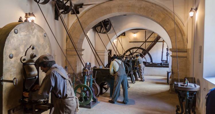Historic industrial workshop with belts and flywheels powering vintage machinery inside arched hall
