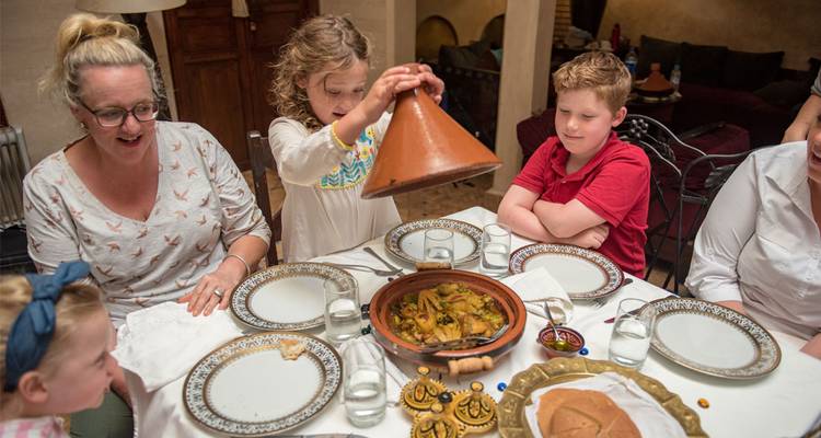 Children and adults gather around a table as a tagine is served during a Moroccan meal.