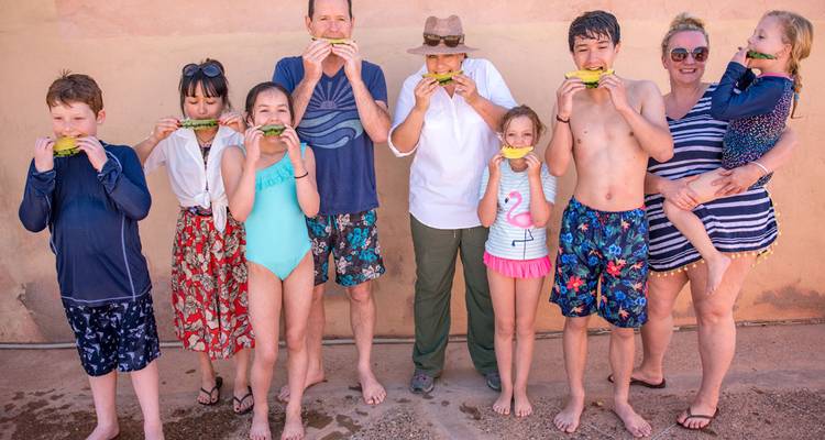 Playful group enjoys watermelon slices against a sun-warmed stucco wall in Morocco.