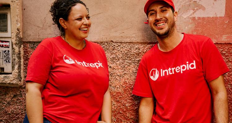 Two tour leaders in matching red Intrepid shirts share a laugh against a textured wall.