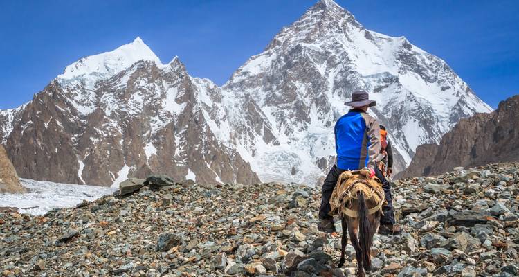 Les trekkers à cheval montent une pente rocheuse en direction des pics enneigés et imposants du Karakoram.