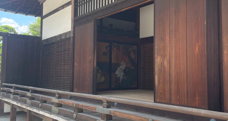 Open sliding doors reveal a tatami room with traditional painted screens inside a wooden temple building.