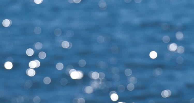 Abstraktes unscharfes Bild von funkelnden Lichtreflexionen auf blauem Wasser.