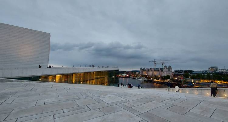 Evening view from sloped roof of Oslo Opera House overlooking harbor lights.