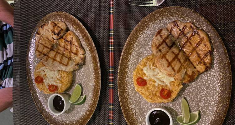 Grilled meat with risotto, lime wedges and sauce presented on a rustic plate in a restaurant
